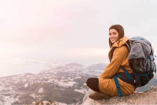 Smiling young woman sitting top of mountain with her backpack