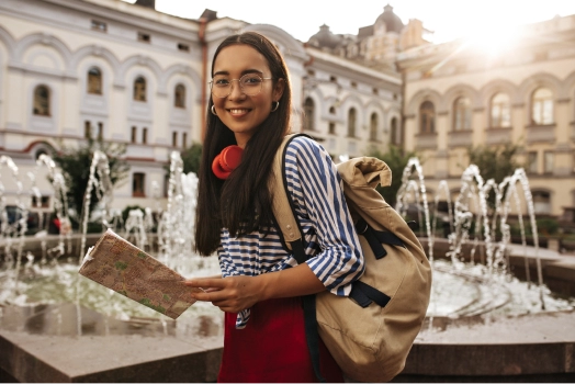 A student with glasses and a backpack holding a map.