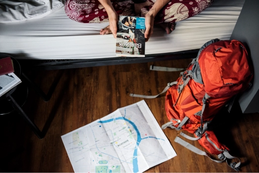 Hands holding a book, beside a backpack and map on the floor.