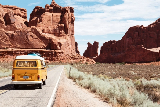 Yellow van traversing a scenic highway winding through rugged mountain terrain.